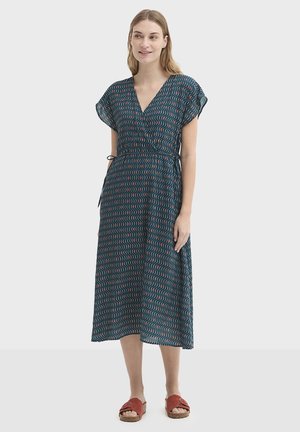 Grønblå kjole med et bølget mønster i rød og hvid, korte flagrende ærmer, dyb V-hals og bånd i taljen, der går til midt på læggen.