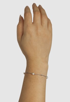 Edelstahlarmband mit kleinen weißen Perlen und Silberperlen, minimalistisches Design an einem verschlossenen Handgelenk. Glatte Textur.