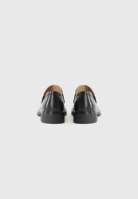 Scarpe in pelle nera con tacco basso, viste da dietro su uno sfondo bianco semplice. Il design è semplice ed elegante.