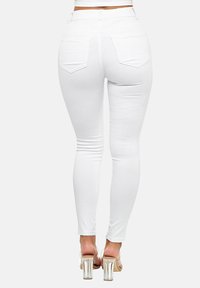 Jeans blancos ajustados con cintura alta, con una textura suave y dos bolsillos traseros. Combinados con zapatos de tacón transparente.