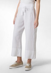 Pantaloni bianchi in lino a gamba larga con vita legata e orli risvoltati, caratterizzati da una morbida texture e una vestibilità rilassata, abbinati a sneakers beige.