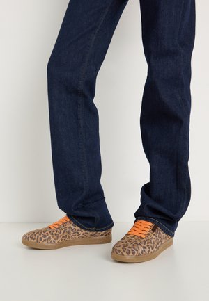 Baskets en imprimé léopard avec des lacets orange, un dessus en tissu texturé et une semelle en caoutchouc brun clair, associées à un jean en denim bleu foncé.