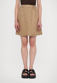 Beige linen mini skirt with a wide belt and a circular buckle. Worn with black platform sandals featuring braided straps and a buckle.