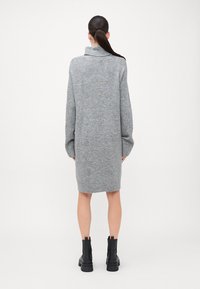 Robe pull surdimensionnée grise avec un col haut, des manches longues et des poignets côtelés, associée à des bottes noires à semelle épaisse.