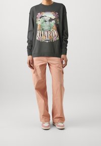 Sudadera gris con gráficos de ondas y flores coloridas. Combinada con pantalones cargo rosa claro. Calzado con diseño en rosa y beige.