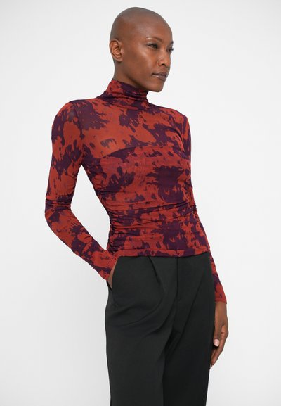 Haut à col roulé ajusté à manches longues dans un motif abstrait rouge et violet, fabriqué en tissu extensible avec des détails froncés sur les côtés.