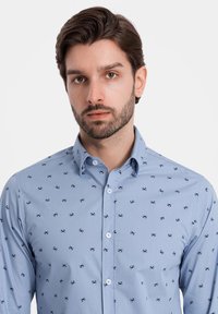 Camisa de botón azul claro con pequeños patrones de cangrejos marinos en color navy, mangas largas y cuello clásico. La tela parece suave con un ligero brillo.