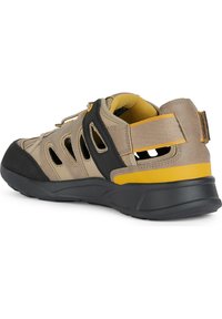 Sandalia ligera con un upper en beige y negro, acentos amarillos, paneles de malla transpirables y una suela de goma texturizada para mayor tracción.