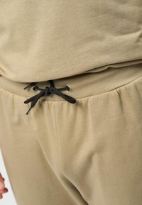Beige katoenen joggers met een zwarte trekkoord in de taille, met elastische boorden en een gladde stoftextuur.