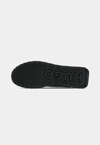 Semelle de chaussure en caoutchouc noir avec des crampons profonds et le mot HUGO embossé en grandes lettres sur le dessous.