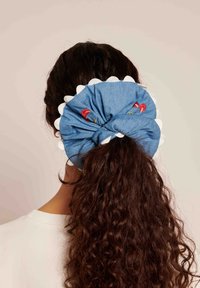 Fita de cabelo em denim azul com bordas brancas em forma de ondas e cerejas vermelhas bordadas. Tecido texturizado com um design em nó.