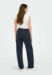 Navyblauwe sweatpants met een relaxte pasvorm en een elastische tailleband, gecombineerd met een witte mouwloze top. Zachte stoftextuur, minimalistisch ontwerp.