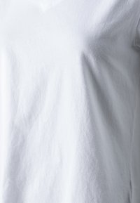Primo piano di una maglietta bianca in cotone a maniche corte che mostra la texture del tessuto e ombre di illuminazione sottili.