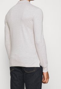 Ljusgrå långärmad polo med strukturerad yta, klassisk krage och sidofickor. I kombination med mörka jeans.