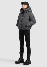 Pelēks pūkains mētelis ar augstu apkakli un regulējamu kapuci, ar priekšējo rāvējslēdzēju un divām lielām kabatām. Valkāts ar melniem legingiem un zābakiem.