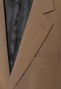 Blazer marrón a medida con una textura suave, con solapas de pico, un bolsillo en el pecho y forro interior negro.