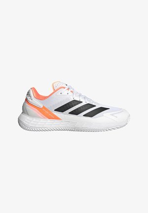 Zapatilla deportiva blanca con rayas negras, detalles en naranja, suela acolchada y texto "Defiant Speed" en el lateral.