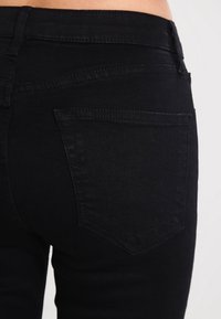 Černé džíny z denimu s těsným střihem, zadními kapsami a hladkou texturou, viditelným švem podél švů.