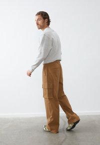 Sudadera gris combinada con pantalones cargo color beige que cuentan con bolsillos laterales y un ajuste relajado; modelo vistiendo calzado multicolor frente a un fondo neutro.