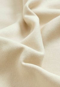 Beige puuvillakangas, sile pind, veidi kortsus ja peene kudumise mustriga, langeb delikaalselt pehmete voltidena.