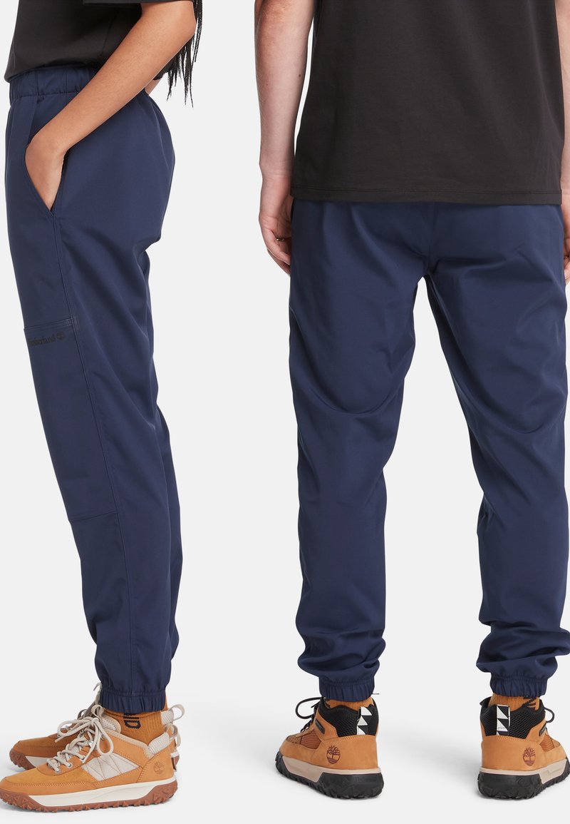Un pantalon bleu marine à taille élastique avec des poches latérales, des chevilles resserrées et un tissu lisse et léger. Conçu pour le confort et la mobilité.