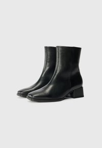 Botas de cuero negras hasta el tobillo con punta cuadrada, textura suave y un tacón bajo de bloque, que presentan un diseño elegante y detalles de costura sencillos.
