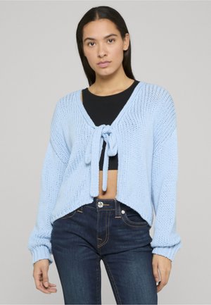Lyseblå strikket cardigan med V-hals og bindebånd foran. Har lange ærmer og en kortet kant med en struktureret strikkemønster.