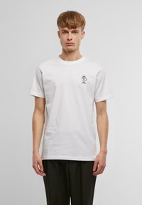 White cotton t-shirt with a round neck, short sleeves, and a small black graphic print on the chest. Simple and unembellished design.