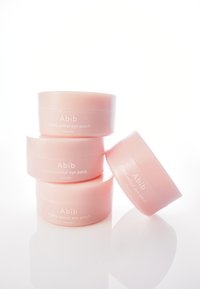 Contenants ronds roses empilés, étiquetés "Abib PDRN patch rétinal pour les yeux", avec des surfaces brillantes et un texte minimal, reflétant la lumière doucement.