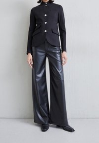Blazer negro ajustado con botones plateados, combinado con pantalones de cuero negros de cintura alta y pierna ancha. Texturas suaves, diseño moderno y a medida.
