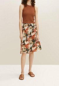Un débardeur marron à côtes associé à une jupe de longueur genou ornée d'un motif floral coloré. Des sandales glissantes marron complètent la tenue.