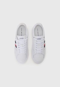 Witte sneaker met een gladde textuur, voorzien van gestyleerde veters, een logo en zwarte en rode strepen aan de zijkanten. Eenvoudig, low-profile ontwerp.
