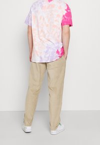 Tričkost s tie-dye ve pastelových barvách růžové, fialové a broskvové, spárované s béžovými kordurovými kalhotami a bílými teniskami s zelenými akcenty.