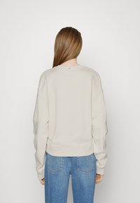 Felpa beige chiaro con vestibilità corta, maniche ampie e orlo a coste. Texture liscia con un piccolo dettaglio sul retro del colletto.