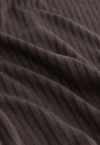 Primer plano de tela de punto acanalada marrón oscura con pliegues suaves y líneas texturizadas verticales visibles.