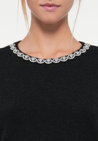 Black knit sweater featuring a scalloped collar adorned with clear embellishments. Close-fitting design with a soft texture.