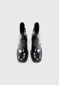 Bottines en cuir noir avec une finition brillante, à bouts carrés, zips sur les côtés et semelles épaisses en caoutchouc, présentant des éléments de design minimalistes.