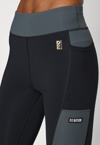 Czarne legginsy z wysokim stanem, kontrastującymi szarymi akcentami, perforowanymi detalami oraz logo P.E Nation z boku.