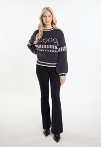 Sweter dzianinowy w ciemnoniebieskim kolorze z jasnymi geometrycznymi wzorami, okrągły dekolt i rękawy w kształcie balonów; połączony z czarnymi spodniami dzwonami i czubkami.