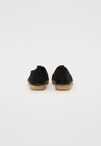 Espadrilles en toile noire avec semelles en jute, arborant un design simple, des coutures contrastantes et des tirettes à l'arrière pour un enfilage facile.