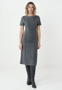 Graues Zweiteiler-Kleid mit kurzen Ärmeln, tailliertem Oberteil und knielangem Rock. Glatte Textur, klare Linien, kombiniert mit knielangen schwarzen Stiefeln.