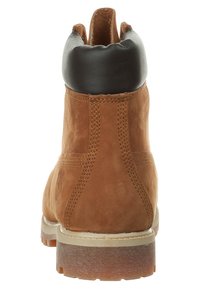 Bottines en daim marron avec un col rembourré noir, une semelle en caoutchouc et une couture contrastante sur les côtés. La vue arrière met en valeur la texture et la forme.