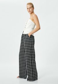 Top blanc sans bretelles avec des boutons sur le devant, associé à un pantalon large à carreaux noir et blanc avec poches et une coupe décontractée.