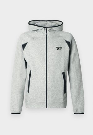 Felpa grigia con zip realizzata in tessuto morbido, dotata di cappuccio, dettagli neri sulle spalle e due tasche laterali con zip. Logo Reebok sul petto.