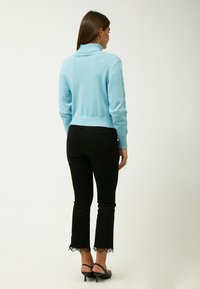 Himmelblaues, gestricktes cropped Sweater mit einem gerippten Rollkragen, kombiniert mit schwarzen ausgestellten Jeans mit Spitzenbesatz am Saum.