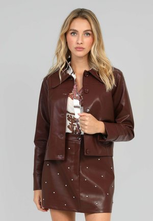 Veste cropped en cuir marron avec un col pointu et une fermeture boutonnée, associée à une jupe assortie ornée de perles argentées.