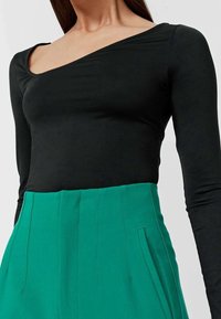 Maglietta nera a maniche lunghe con scollo asimmetrico abbinata a pantaloni verdi a vita alta con pince e tasche laterali.