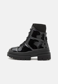 Bottes chevilles en cuir verni noir avec une semelle épaisse, un col en tricot et un laçage à l'avant. Présente une texture lisse et de subtils détails en panneaux.