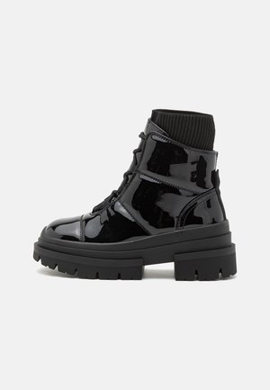 Melna patentēta ādas potītes zābaki ar masīvu zoli, adītu apkakli un auklu aizdari. Iespējama gluda tekstūra un izsmalcināta paneļu detaļošana.