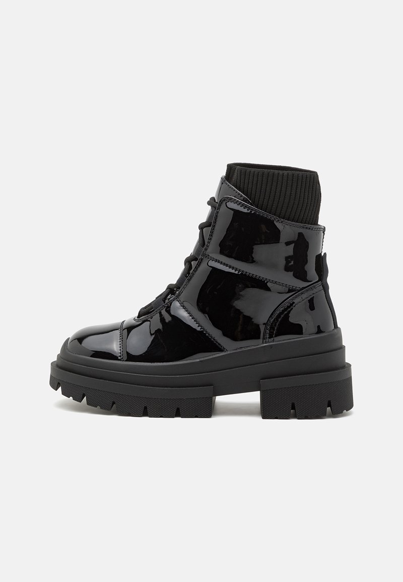 Bottes chevilles en cuir verni noir avec une semelle épaisse, un col en tricot et un laçage à l'avant. Présente une texture lisse et de subtils détails en panneaux.